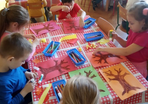 Dzieci ozdabiają drzewa liśćmi z kolorowego papieru.