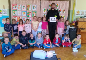Dzieci pozują że strażakiem, przed nimi leży fantom do ćwiczeń z pierwszej pomocy