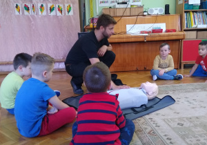 Dzieci obserwują strażaka demonstrującego na fantomie jak udzielać pierwszej pomocy