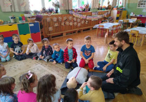 Dzieci obserwują strażaka demonstrującego na fantomie jak udzielać pierwszej pomocy