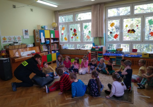 Dzieci obserwują strażaka demonstrującego na fantomie jak udzielać pierwszej pomocy
