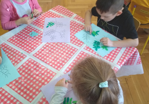 Dzieci wyklejają zielona plastelina i kulkami z czerwonej bibuły kontur gałązki jarzębiny