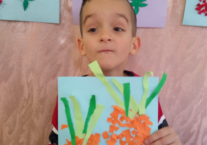 Chłopiec prezentuje swoją pracę- marchewki z wydzieranki