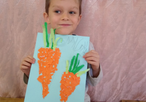 Chłopiec prezentuje swoją pracę- marchewki z wydzieranki