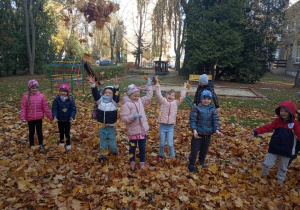 Dzieci śmieją się i podrzucają liście do góry.