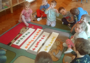 dzieci siedzą na dywanie przy kolorowych listkach