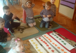 dzieci siedzą na dywanie przy kolorowych listkach