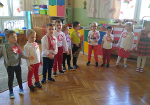 Dzieci ubrane w stroje w kolorach białym i czerwonym śpiewają piosenkę