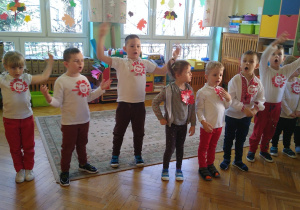 Dzieci ubrane w stroje w kolorach białym i czerwonym śpiewają piosenkę