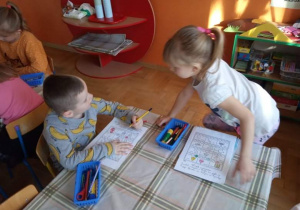 Dzieci wykonują karty pracy przy stoliku