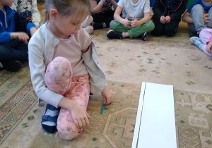 Dziewczynka układa patyczki na dywanie.