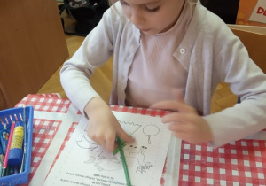 Dziewczynka koloruje obrazki zgodnie z odczytywanym poleceniem.
