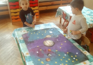 dzieci doklejają gwiazdki i planety na namalowany karton