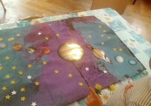 dzieci doklejają gwiazdki i planety na namalowany karton