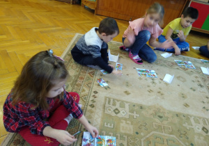 Dzieci na dywanie układają historyjkę obrazkową.