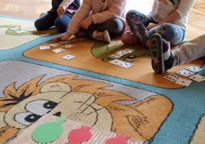 dzieci siedzą na dywanie. na dywwanie leżą karteczki z cyframi