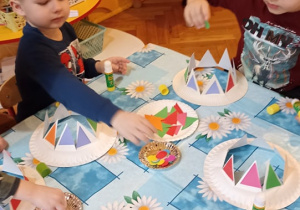 dzieci prezentują czpki karnawałowe wykonane z talerzyków papierowych
