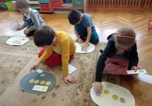 Dzieci układają różne sumy z papierowych monet.