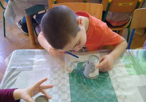 Chłopiec maluje papierowy kubek na szaro