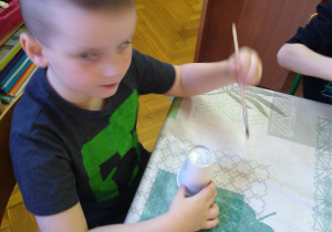 Chłopiec maluje papierowy kubek na szaro