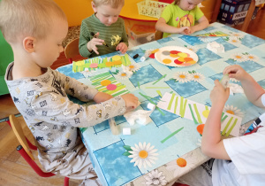 dzieci przy stole naklejają elementy z kolorowego papieru