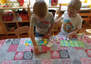 dzieci przy stole naklejają elementy z kolorowego papieru