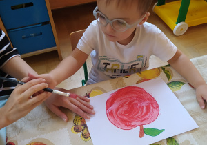 Chłopczyk maluje jabłko czerwoną farbą.