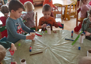 dzieci oklejają papierem kolorowym rolkę