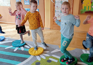 dzieci stoją na jednej nodze na kolorowym krążku