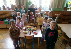 Dzieci pozują przy stole, na którym stoją talerze z pokrojonymi owocami