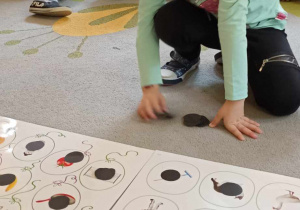 dzieci układają czarne kółka na planszy z obrazkami
