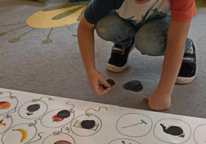 dzieci układają czarne kółka na planszy z obrazkami
