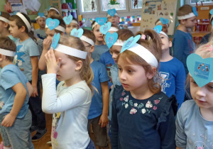 dzieci stoją , na głowach mają opaski z niebieskim serduszkiem