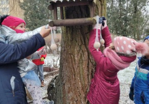 Dzieci wkładają jedzenie do karmników.