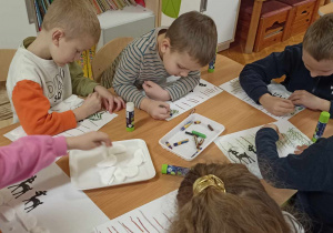dzieci siedzą przy stole i rysują choinki
