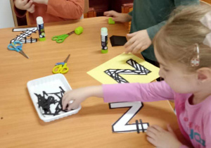 dzieci wyklejają literę z czarnymi paskami