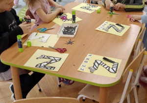 dzieci wyklejają literę z czarnymi paskami