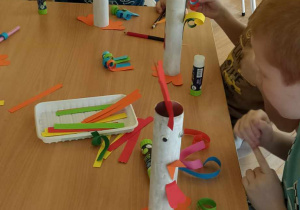 dzieci doklejają elementy z papieru kolorowego do rolki