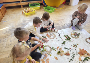 Dzieci wyklejają koszyczek przy pomocy naturalnych materiałów