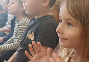 dzieci siedzą na ławce i klaszczą