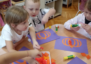 dzieci wyklejają bibułą sylwetę dyni