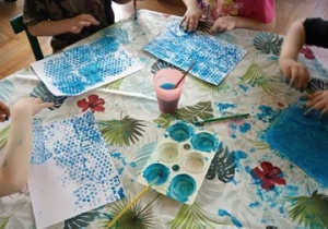 Dzieci odbijają niebieską farbę na kartkach papieru.