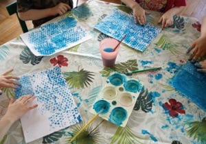 Dzieci odbijają niebieską farbę na kartkach papieru.