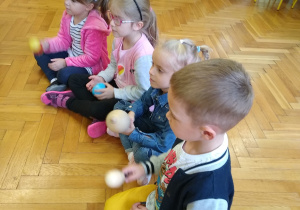 Dzieci siedzą na podłodze, trzymają instrumenty perkusyjne