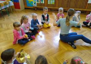 Dzieci siedzą na podłodze, trzymają instrumenty perkusyjne