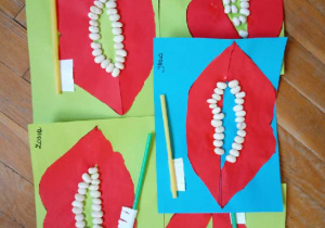 Prace plastyczne przedstawiające papierowe usta i "zęby" naklejone z fasol