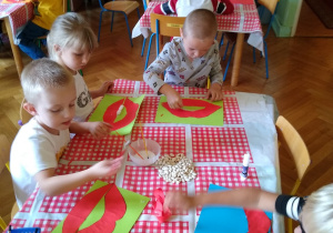 Dzieci wycinają usta z kartki, czerwonego papieru, naklejają fasolę