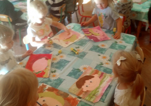 dzieci siedzą przy stole i naklejają kolorowe elementy z papieru
