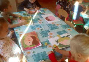 dzieci siedzą przy stole i naklejają kolorowe elementy z papieru