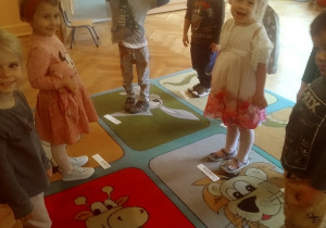 dzieci stoją na dywanie przy swoich wizytówkach